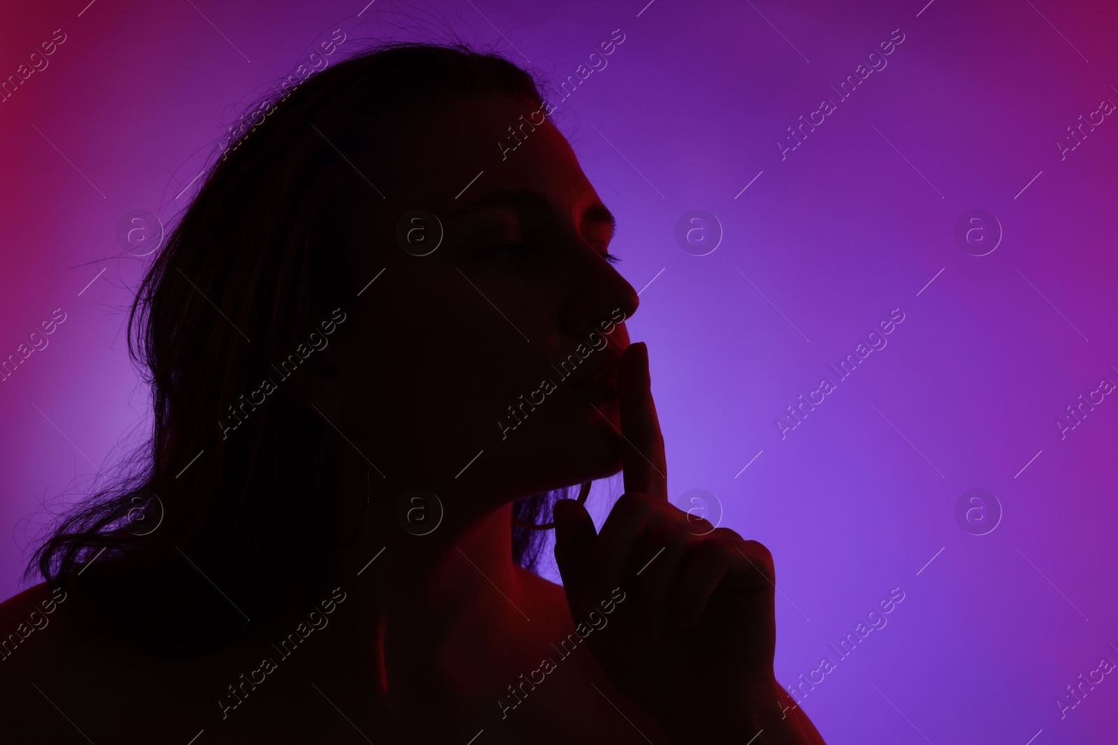 Silhouette of woman making silent gesture in neon lights on color background, space for text Photo of Silhouette of woman making silent gesture in neon lights on color background, space for text