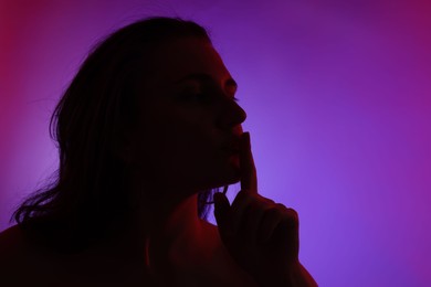 Photo of Silhouette of woman making silent gesture in neon lights on color background, space for text