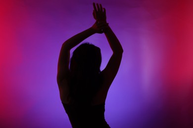 Photo of Silhouette of woman posing in neon lights on color background, back view