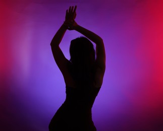 Photo of Silhouette of woman posing in neon lights on color background, back view