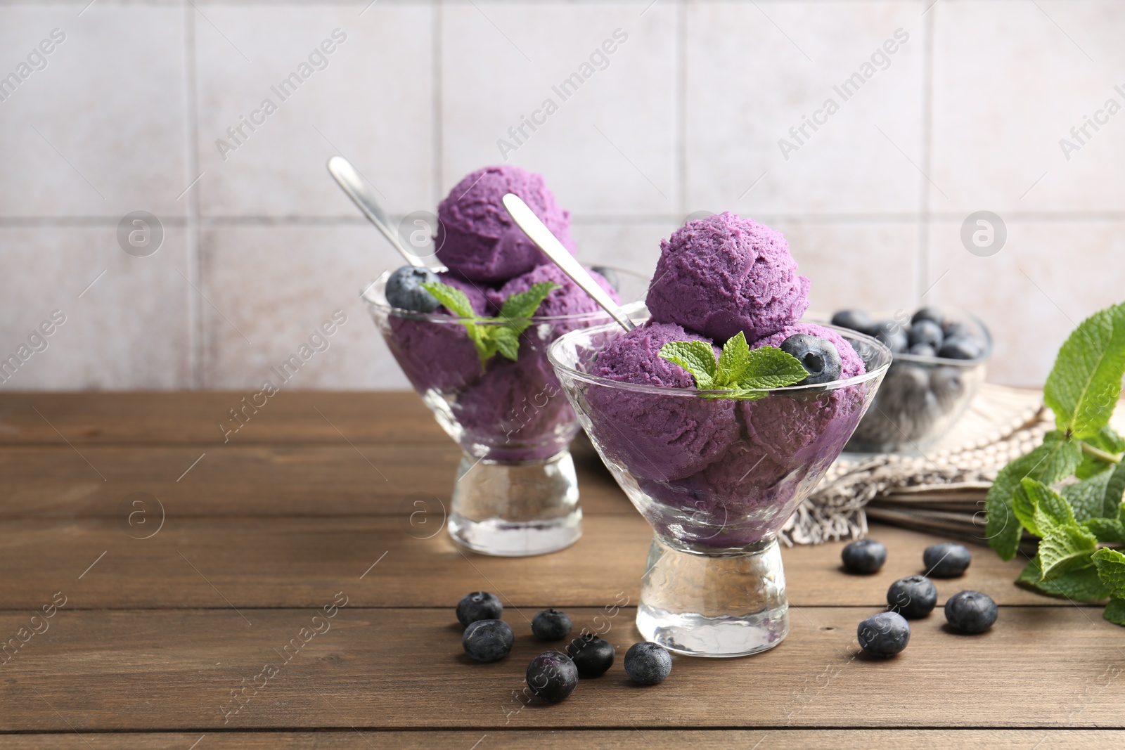 Tasty sorbet with blueberries and mint in dessert bowls on wooden table against tiled background, closeup Photo of Tasty sorbet with blueberries and mint in dessert bowls on wooden table against tiled background, closeup