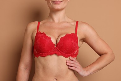 Photo of Woman wearing beautiful red bra on beige background, closeup