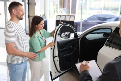 Photo of Salesman with clipboard showing new car to happy family in salon, closeup