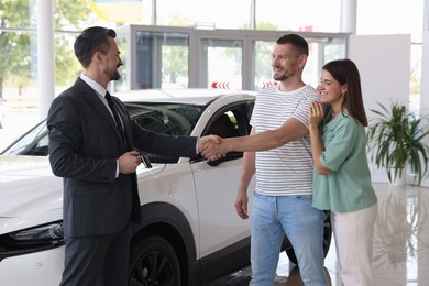 Photo of Salesman shaking hands with happy family near new car in salon