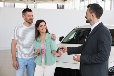 Photo of Smiling salesman giving car key to happy family in salon