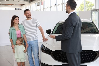 Photo of Salesman showing new car to happy family in salon