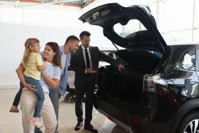 Photo of Salesman showing new car to happy family in salon