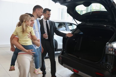 Photo of Salesman showing new car to happy family in salon