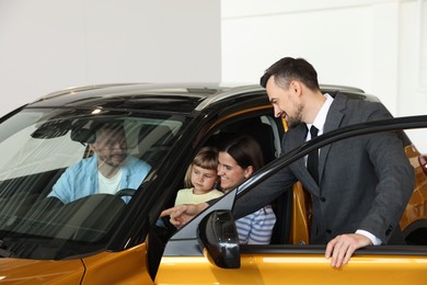 Photo of Salesman showing new car to happy family in salon