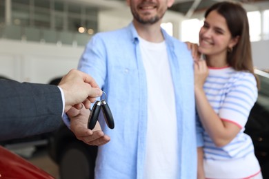 Photo of Salesman giving car key to happy family in salon, selective focus