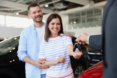 Photo of Salesman giving car key to happy family in salon, selective focus