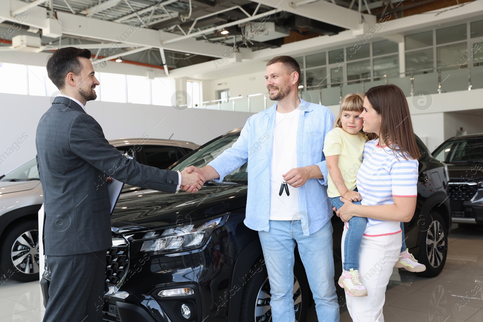 Salesman shaking hands with happy family near new car in salon Photo of Salesman shaking hands with happy family near new car in salon