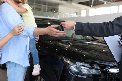 Photo of Salesman giving car key to family in salon, closeup