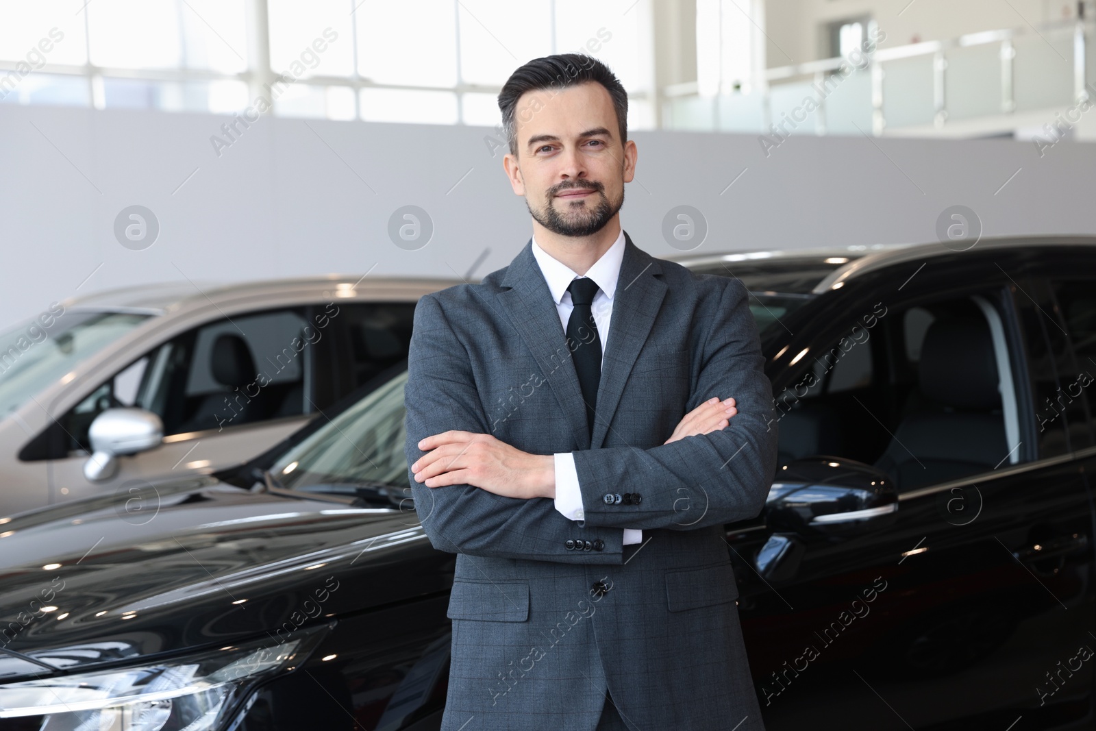 Photo of Portrait of salesman with crossed arms near new car in salon