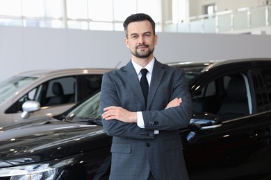 Photo of Portrait of salesman with crossed arms near new car in salon