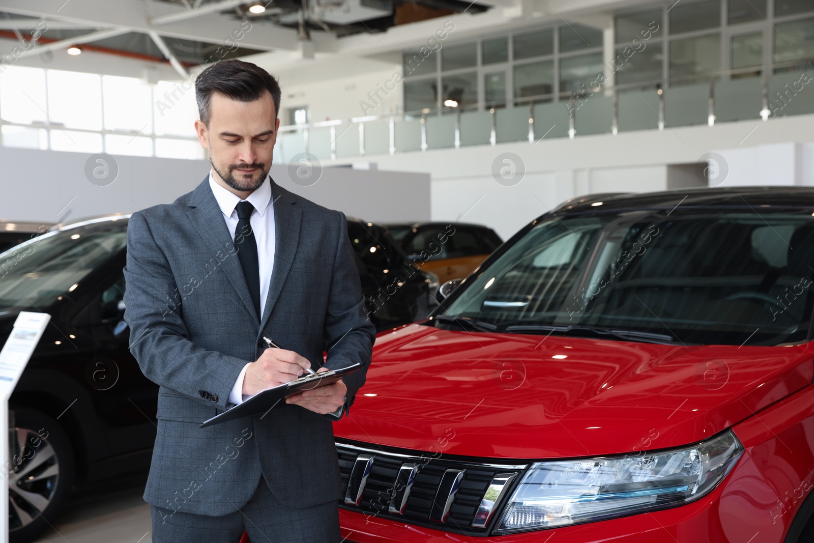 Salesman working with clipboard near new car in salon Photo of Salesman working with clipboard near new car in salon