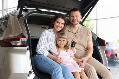 Photo of Happy family with keys sitting in car trunk in salon