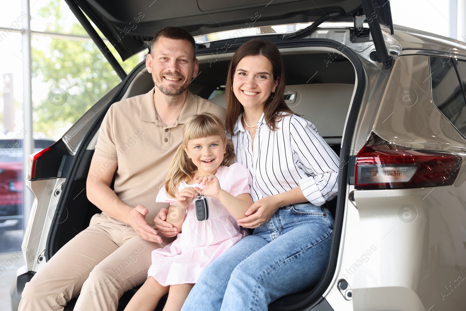 Photo of Happy family with keys sitting in car trunk in salon