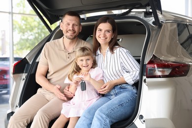 Photo of Happy family with keys sitting in car trunk in salon