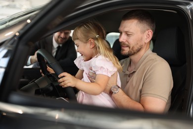 Photo of Happy family holding steering wheel inside new car and salesman, selective focus