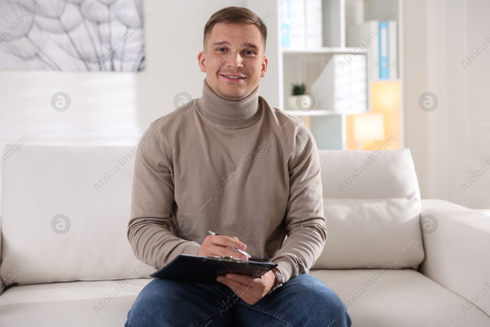 Photo of Portrait of smiling psychologist with clipboard on sofa in office