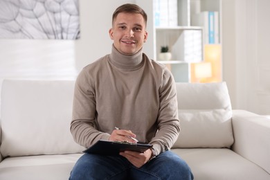 Photo of Portrait of smiling psychologist with clipboard on sofa in office