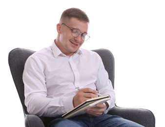 Photo of Smiling psychologist in glasses with notepad sitting on armchair against white background