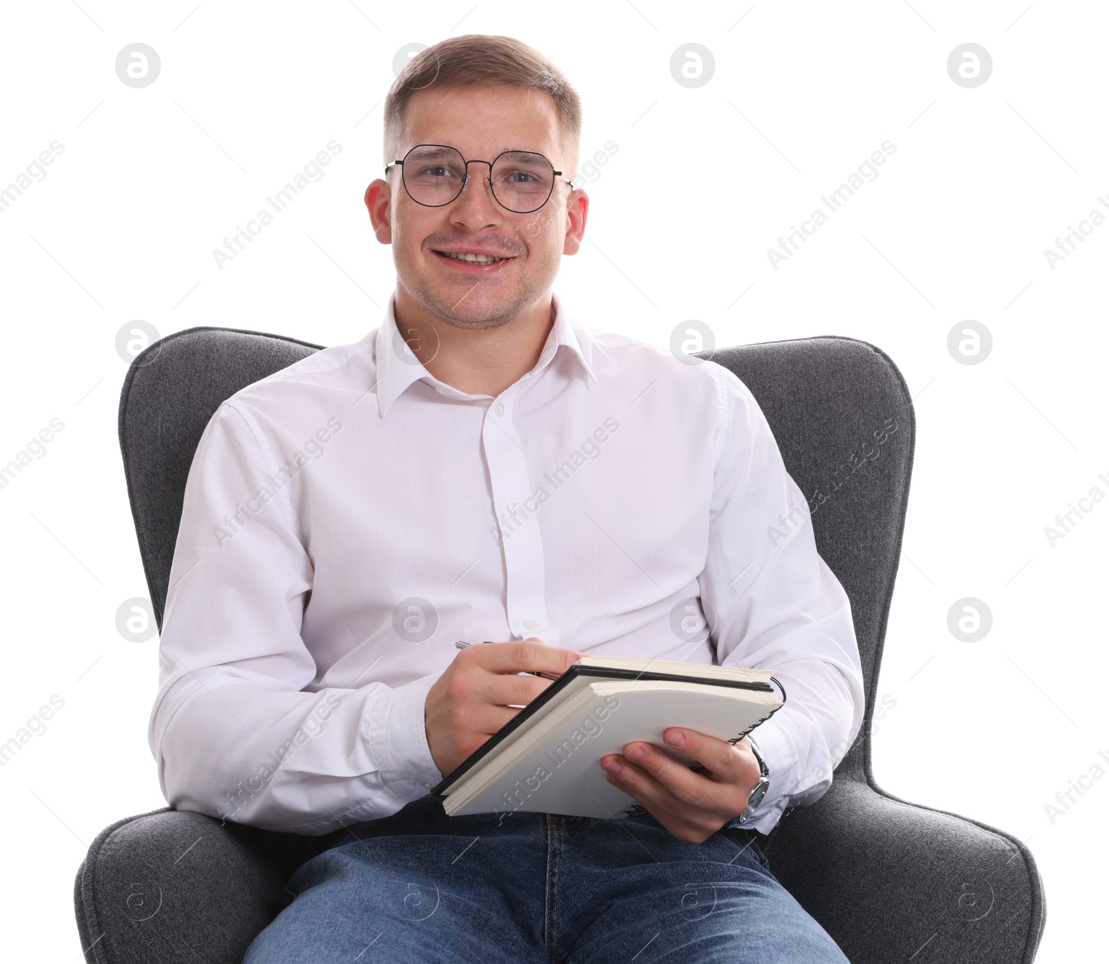 Smiling psychologist in glasses with notepad sitting on armchair against white background Photo of Smiling psychologist in glasses with notepad sitting on armchair against white background