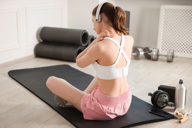 Photo of Sports injury. Young woman suffering from shoulder pain in fitness studio, back view