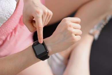 Photo of Woman checking fitness tracker during training indoors, closeup