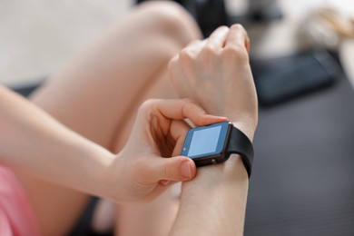 Photo of Woman checking fitness tracker during training indoors, closeup
