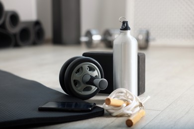 Photo of Phone and different fitness equipment on floor in gym, closeup