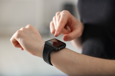 Photo of Woman checking fitness tracker during training indoors, closeup
