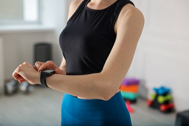 Photo of Woman checking fitness tracker during training indoors, closeup