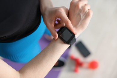 Photo of Woman checking fitness tracker during training indoors, above view