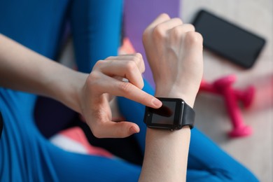 Photo of Woman checking fitness tracker during training indoors, closeup