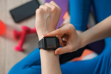 Photo of Woman checking fitness tracker during training indoors, closeup