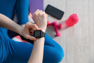 Photo of Woman checking fitness tracker during training indoors, closeup