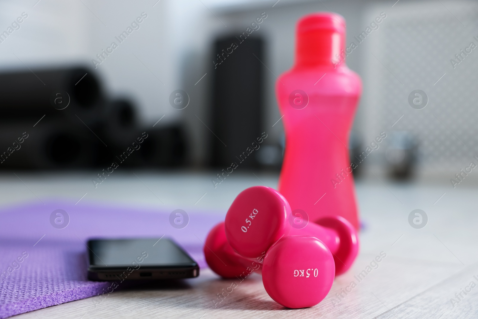 Photo of Water bottle, dumbbells, fitness mat and phone in gym, closeup