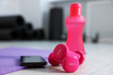 Photo of Water bottle, dumbbells, fitness mat and phone in gym, closeup