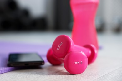 Photo of Water bottle, dumbbells, fitness mat and phone in gym, closeup