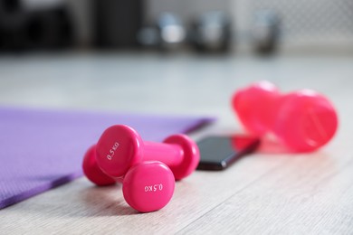 Photo of Water bottle, dumbbells, fitness mat and phone in gym, closeup