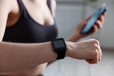 Photo of Woman checking fitness tracker during training indoors, closeup
