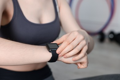Photo of Woman checking fitness tracker during training indoors, closeup