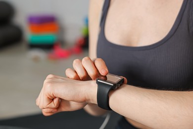Photo of Woman checking fitness tracker during training indoors, closeup
