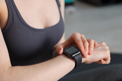 Photo of Woman checking fitness tracker during training indoors, closeup