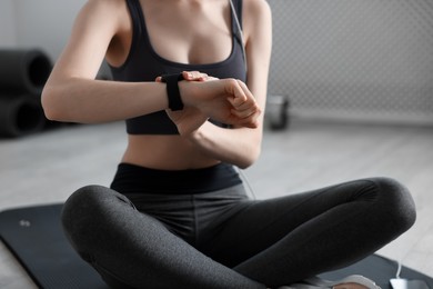 Photo of Woman checking fitness tracker during training indoors, closeup