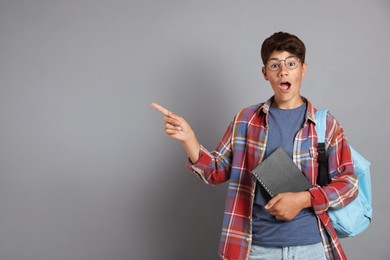 Photo of Teenage boy with notebook and backpack pointing at something on grey background, space for text
