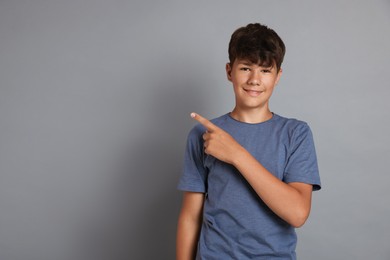 Photo of Teenage boy pointing at something on grey background, space for text