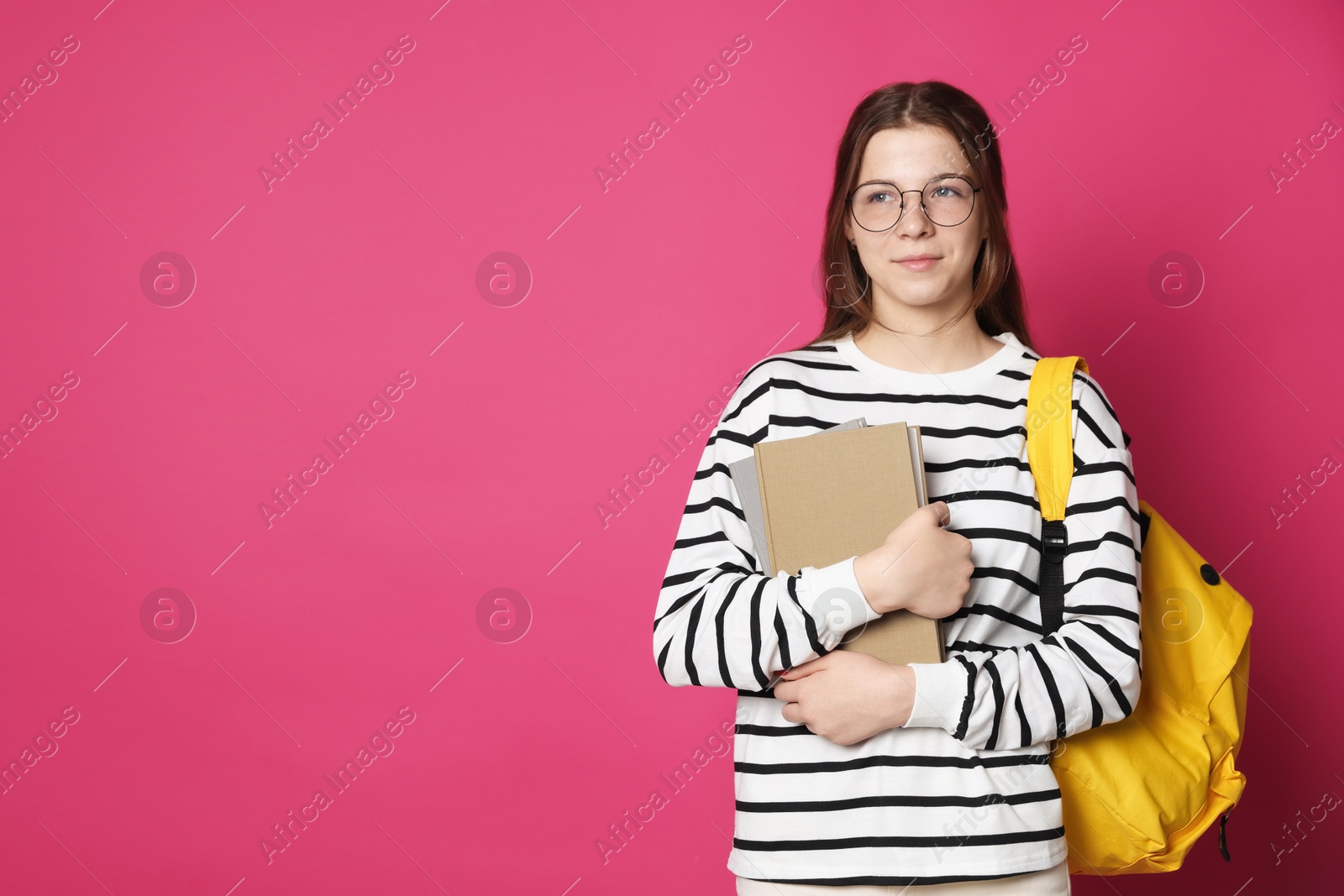 Teenage girl in glasses with backpack and books on crimson background, space for text Photo of Teenage girl in glasses with backpack and books on crimson background, space for text